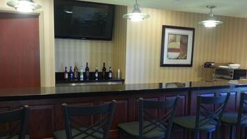 A bar area with a counter displaying bottles, a television mounted on the wall, and a framed picture.