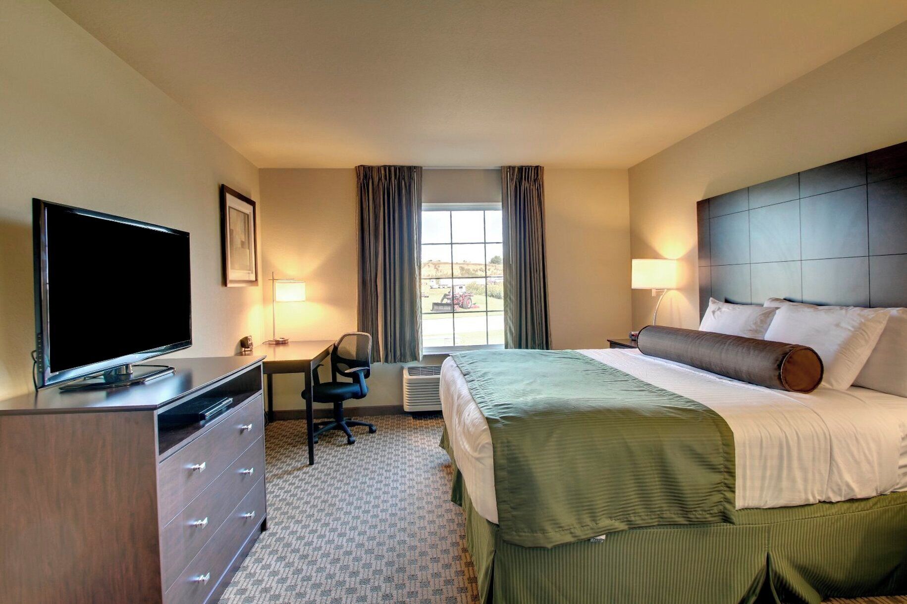 A hotel room with a bed, a desk, a chair, a television, and a dresser.