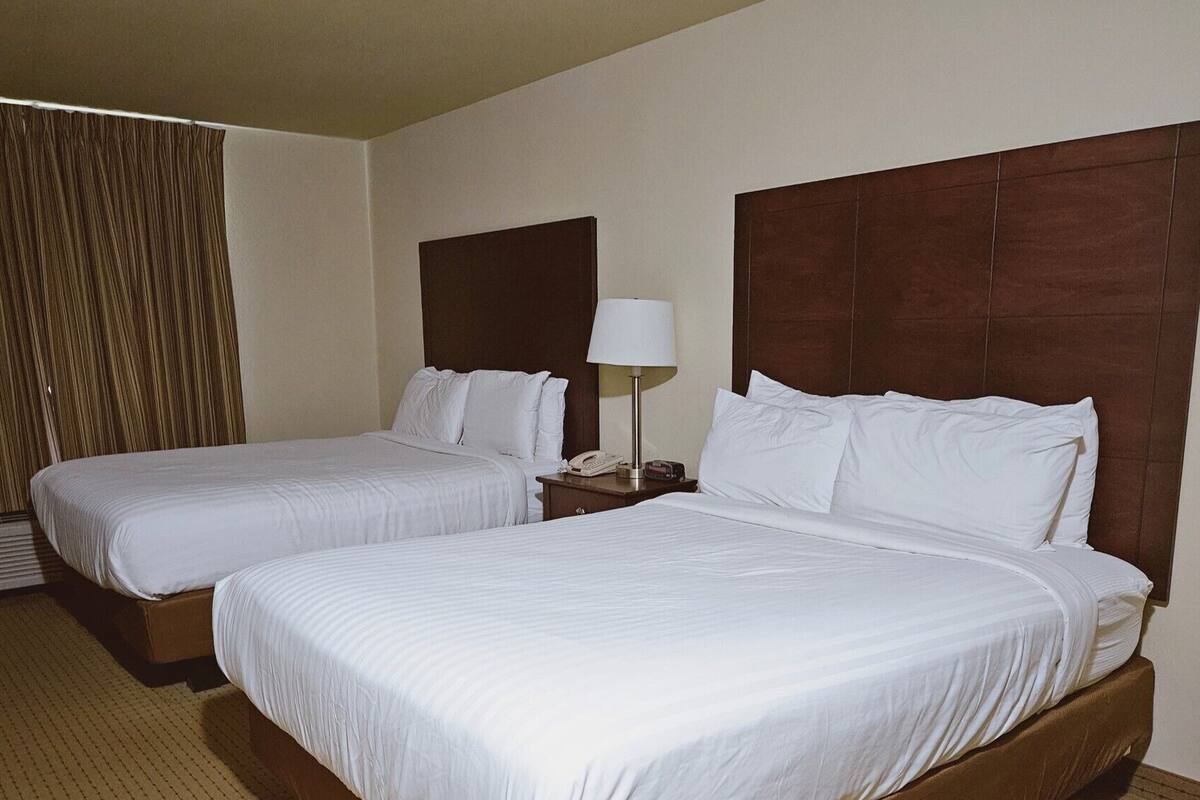 A hotel room with two single beds, a nightstand with a lamp, and a large window with curtains.