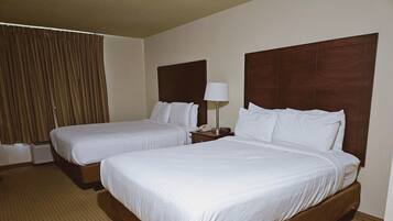 Habitación de hotel con dos camas individuales, una mesita de noche con lámpara y un ventanal con cortinas.