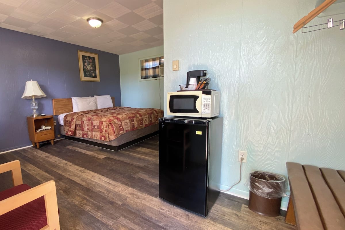 A room with a bed, a desk, a chair, a microwave, and a trash can.