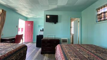A room with two beds, a desk, a chair, a television, and a door.
