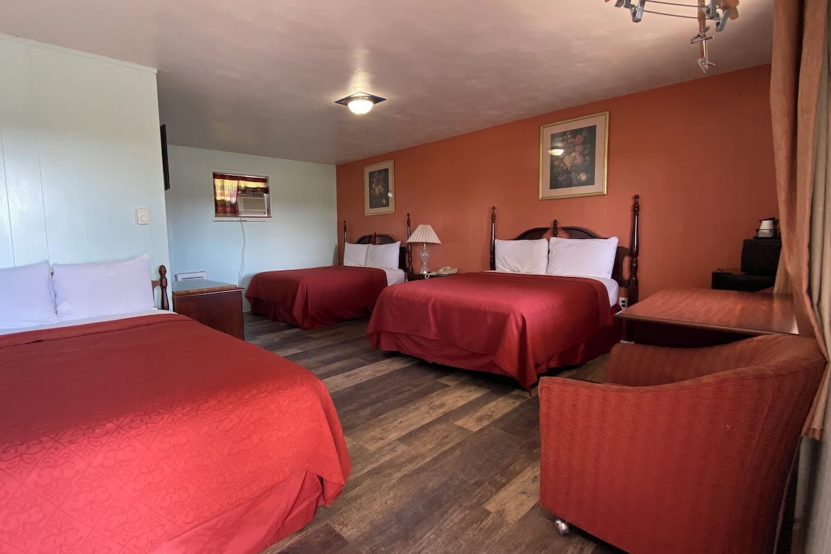 A hotel room with two beds, a wooden floor, a ceiling light, and a framed picture on the wall.