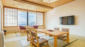 Ein traditioneller japanischer Raum mit Tatami-Boden, einem Holztisch, Stühlen, einem Fernseher und Blick durch große Fenster.