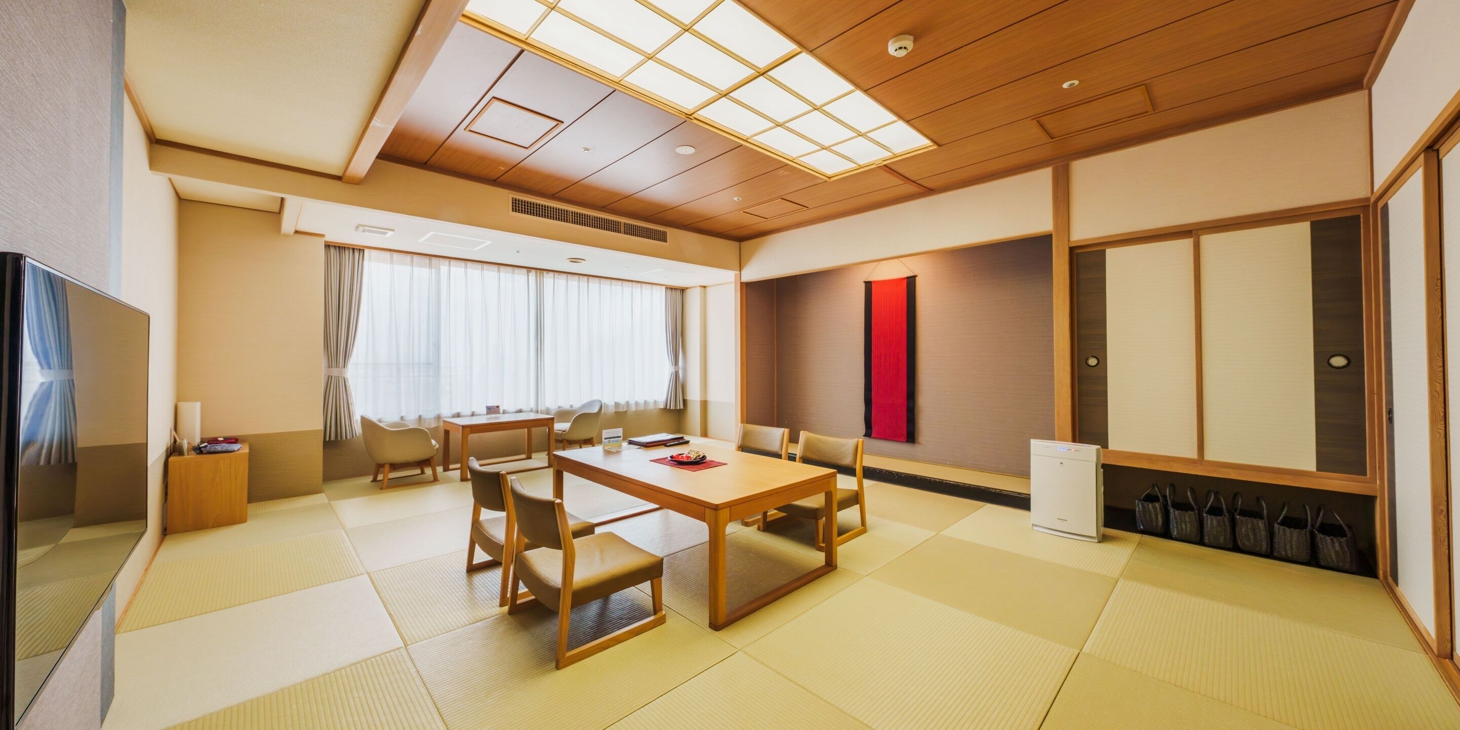 A traditional Japanese-style room with tatami flooring, a low table with chairs, a television, and sliding doors.