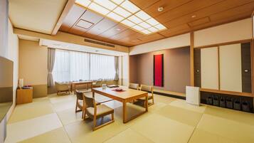 A traditional Japanese-style room with tatami flooring, a low table with chairs, a television, and sliding doors.