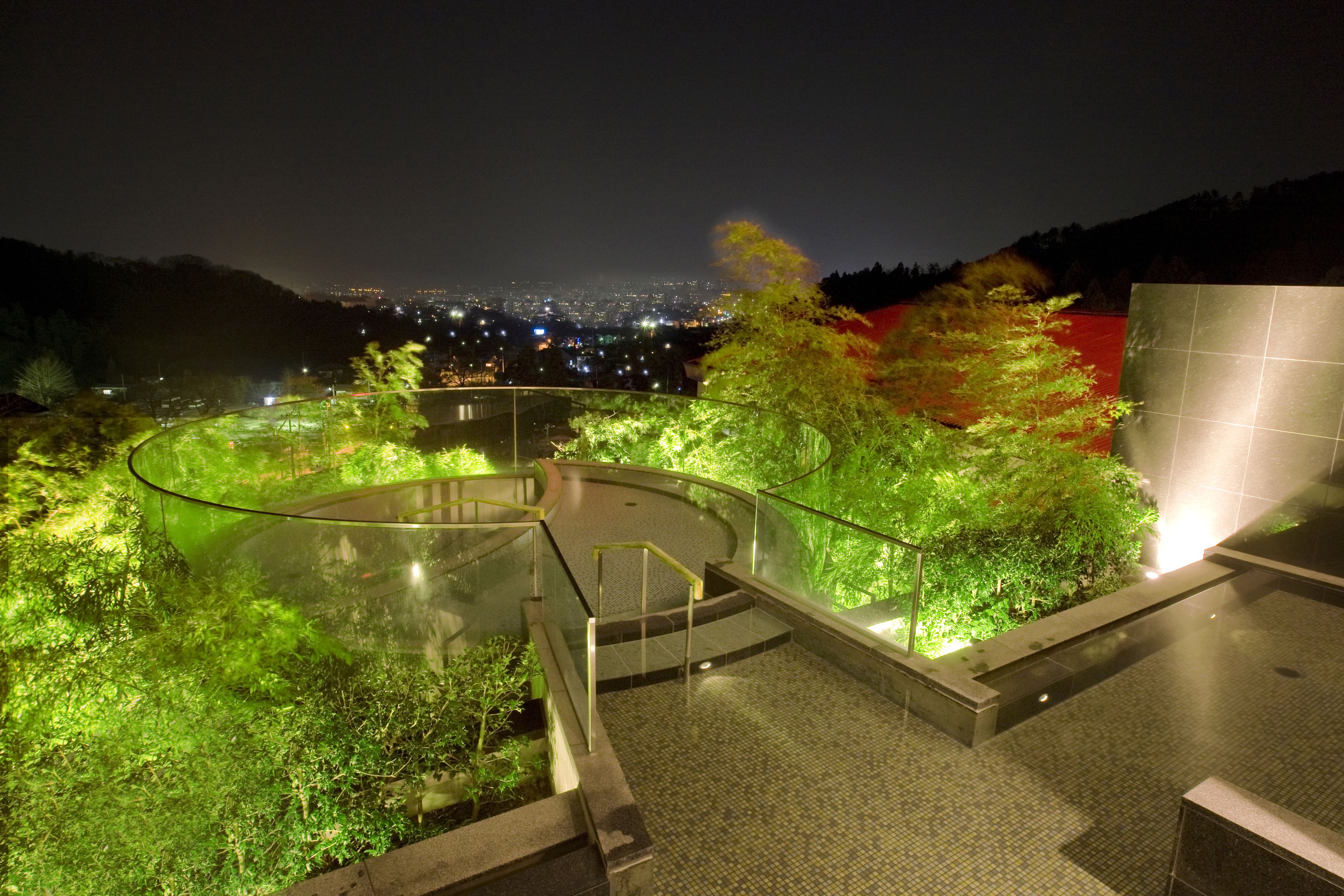 A rooftop garden with a glass balustrade, a small pool, and a view of a cityscape at night.