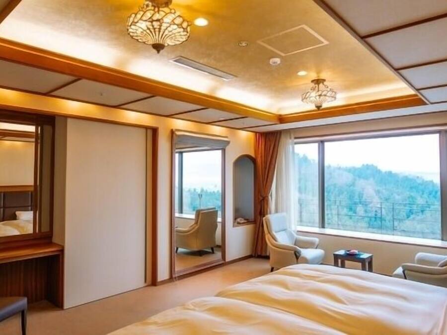 A hotel room with a large bed, a desk, two chairs, a mirror, and a view of the outdoors.