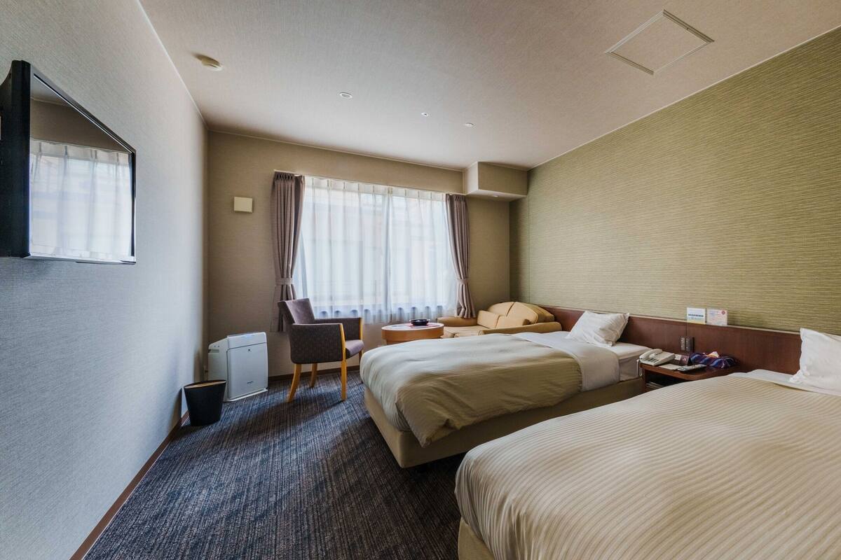 Habitación de hotel con dos camas, un escritorio, una silla, una ventana con cortinas y un televisor de pantalla plana.