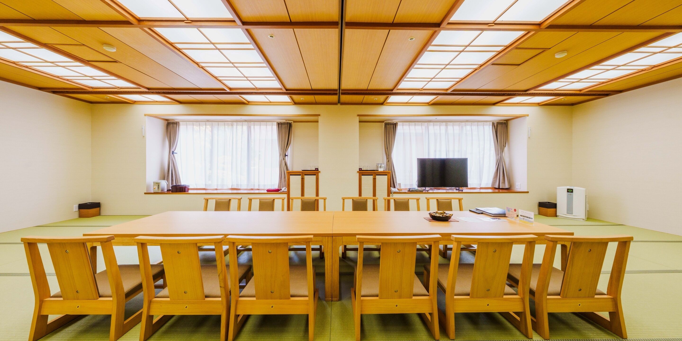A conference room with a long table and chairs, large windows with curtains, and a ceiling with wooden panels.