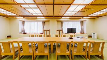 A conference room with a long table and chairs, large windows with curtains, and a ceiling with wooden panels.