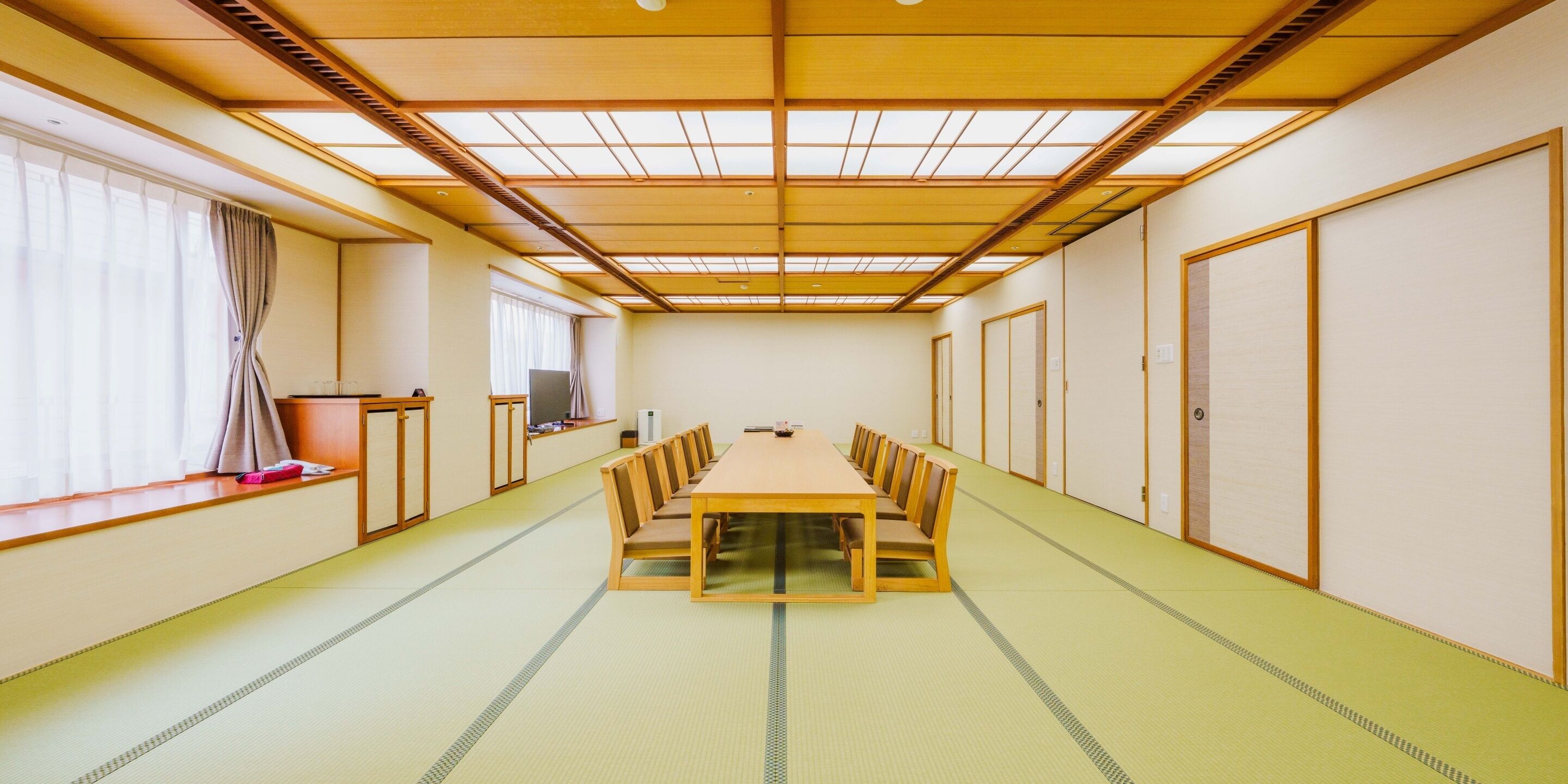 A traditional Japanese room with tatami flooring, a long wooden table, and sliding doors.