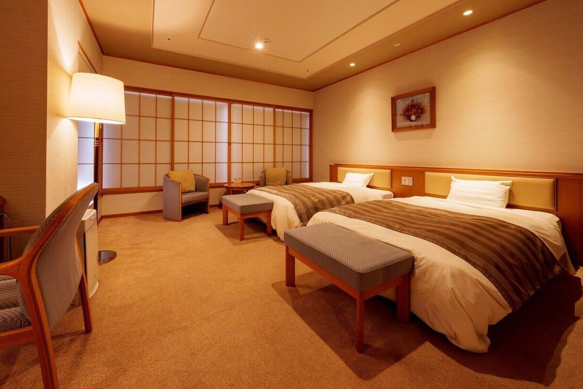 Una habitación de hotel con una puerta corredera de estilo japonés tradicional, una cama con cabecera de madera, un escritorio con silla y una mesita con lámpara.