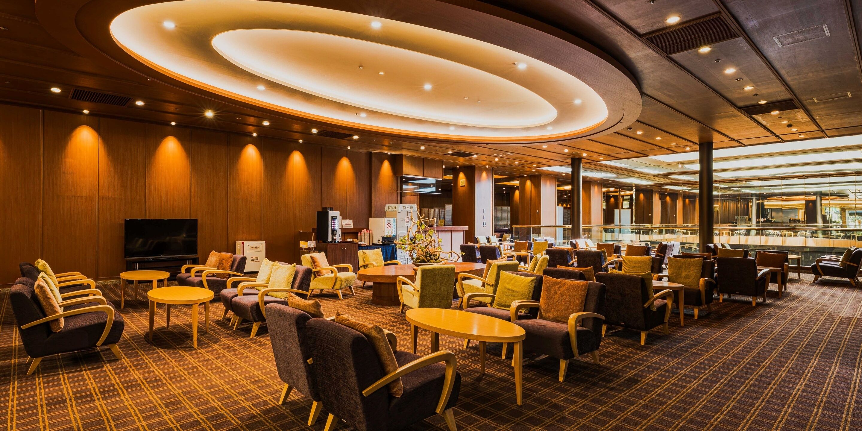 A hotel lobby with a central seating area, a television, and a reception desk.