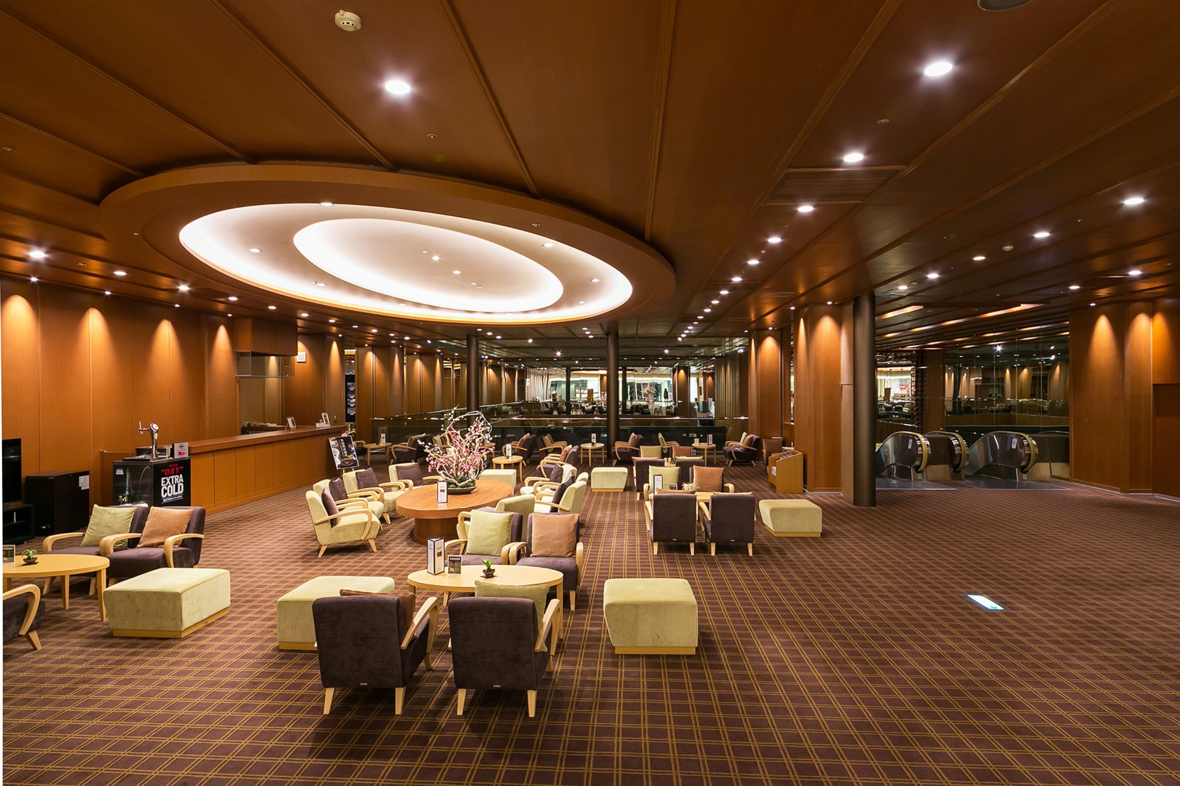 A spacious lobby with a central seating area, multiple tables, and a large, circular light fixture on the ceiling.