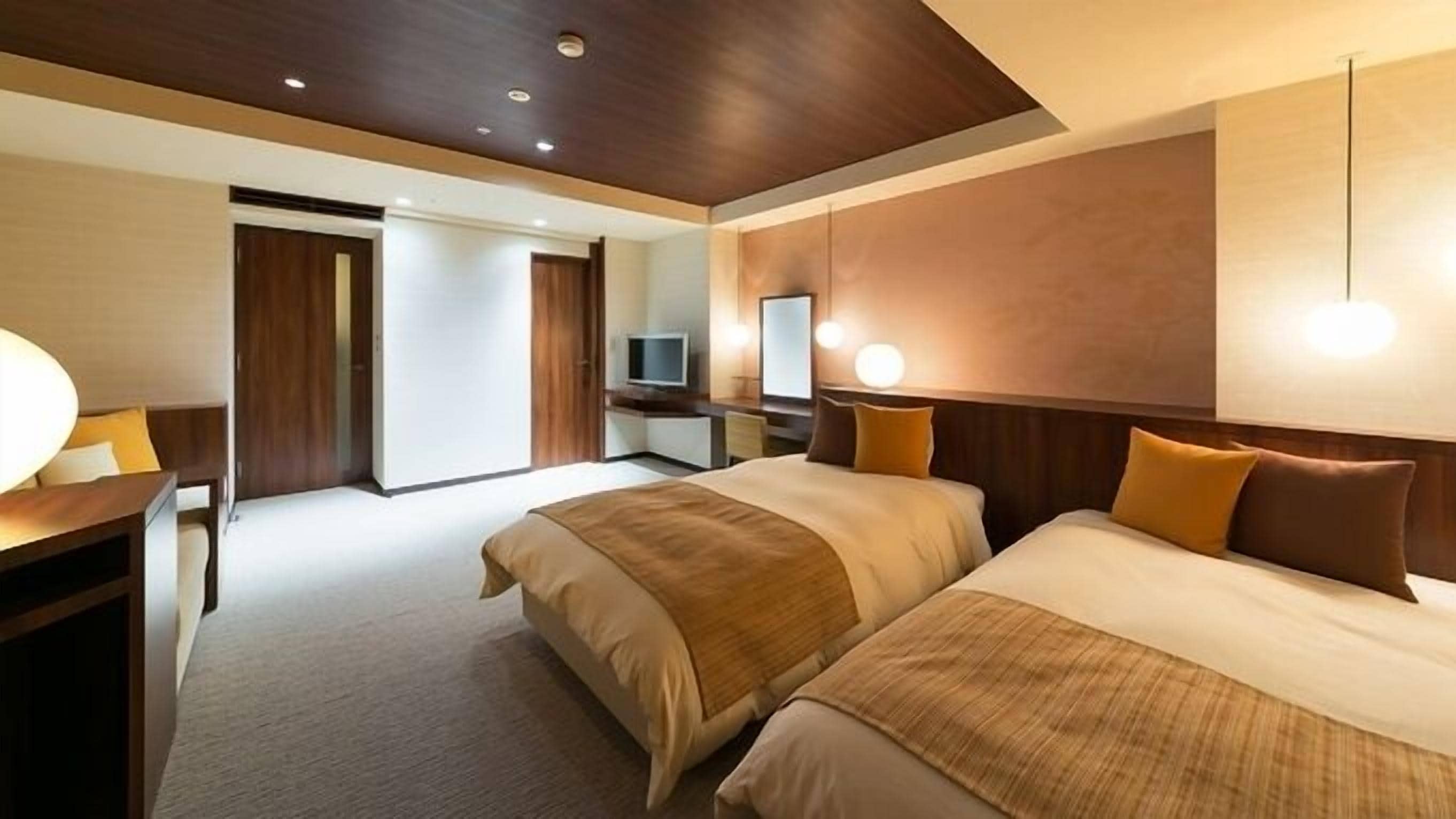 A hotel room with two beds, a desk, a TV, and a mirror.