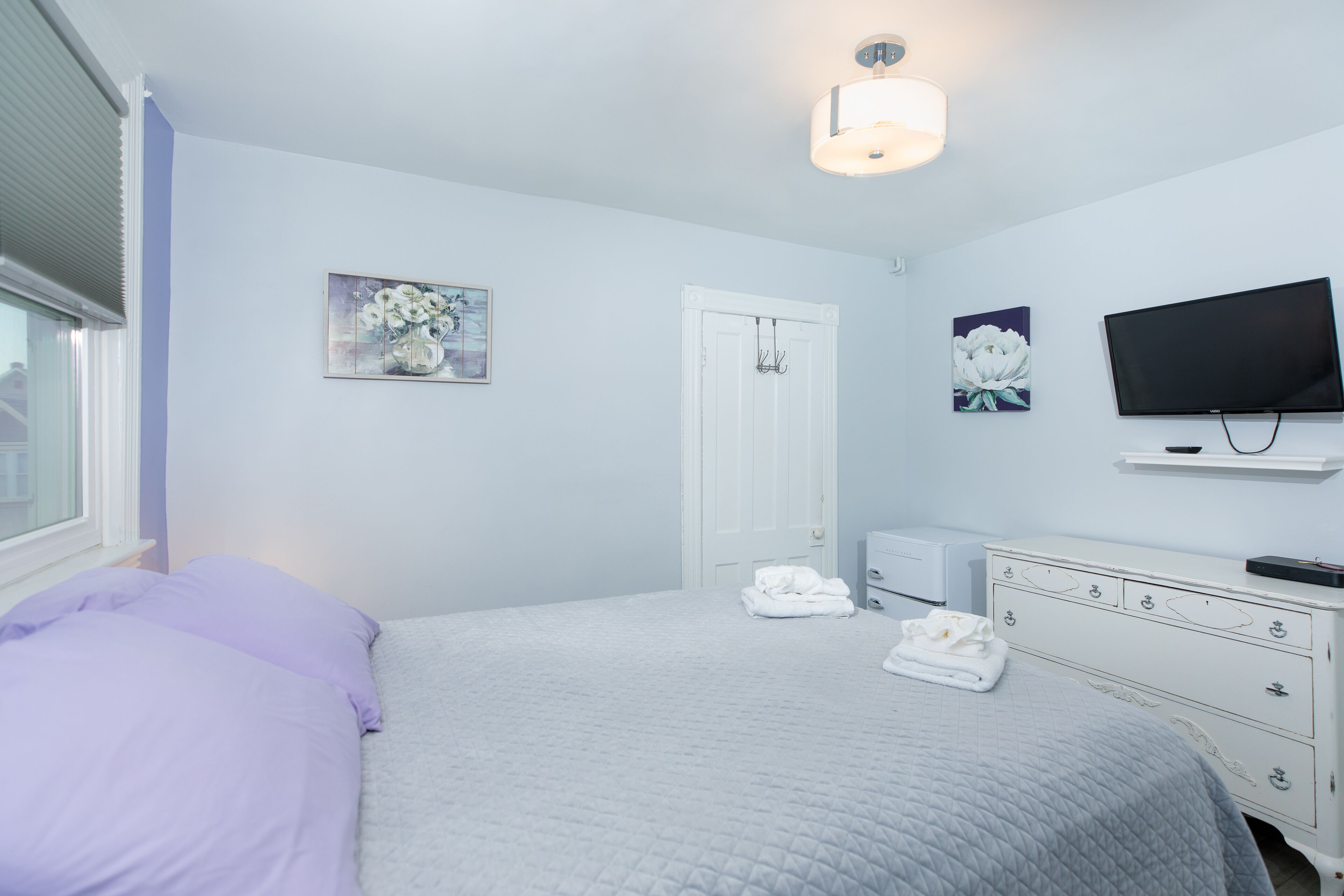 Un dormitorio con cama, cómoda, televisor y puerta.