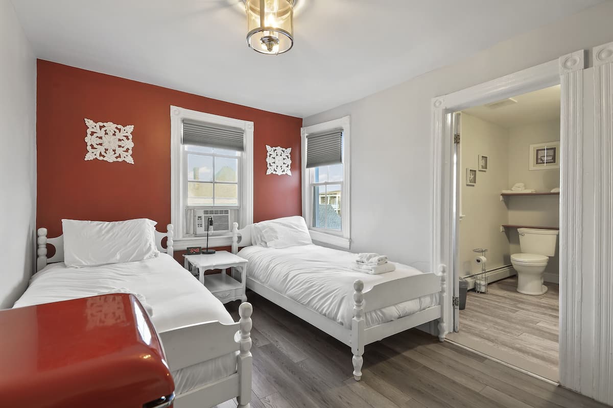A bedroom with two beds, a desk, and a bathroom visible through an open door.
