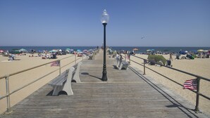 A wooden boardwalk leading to a beach with umbrellas and American flags. - The Inn at Ocean Grove (Ocean Grove)