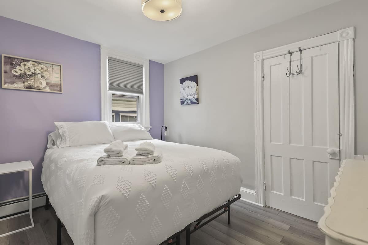 A bedroom with a bed, a nightstand, a door, and a window.