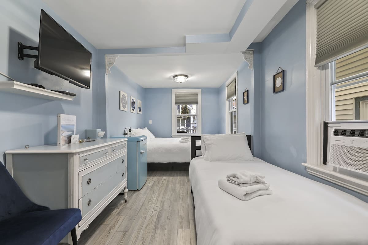 A hotel room with a bed, a desk, a chair, a TV, and a window with blinds.