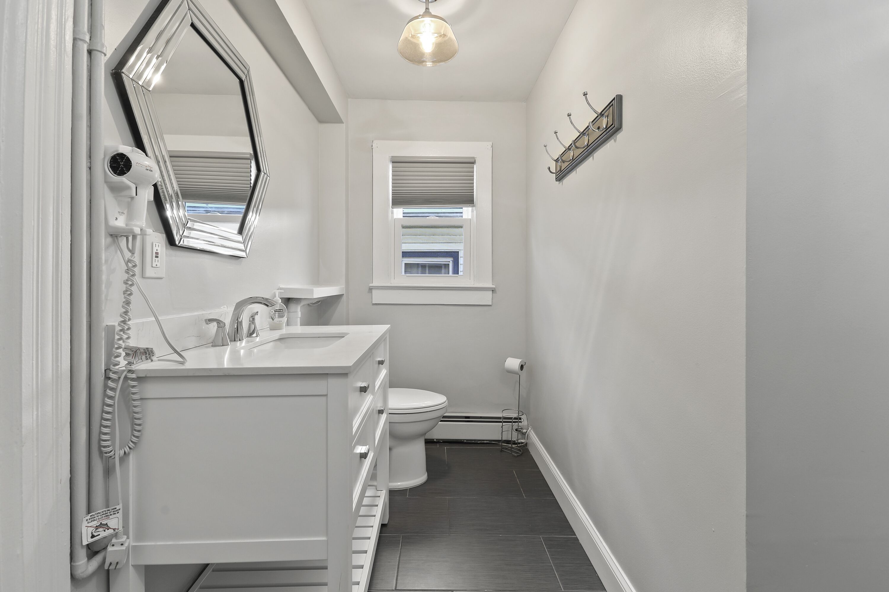 A modern bathroom with a vanity, toilet, and a window with blinds.