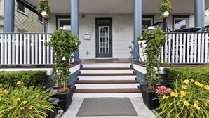 A front entrance with a wooden staircase, white railings, and potted plants. - The Inn at Ocean Grove (Ocean Grove)
