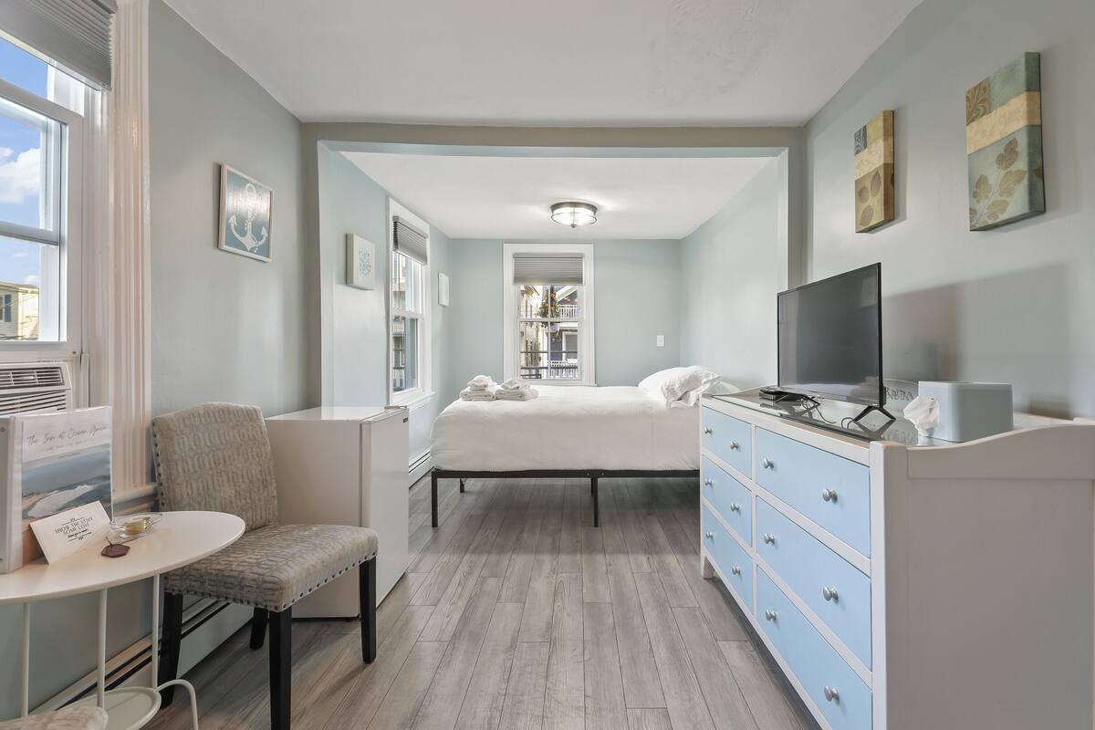 A bedroom with a bed, a TV, a dresser, a chair, and a small table.