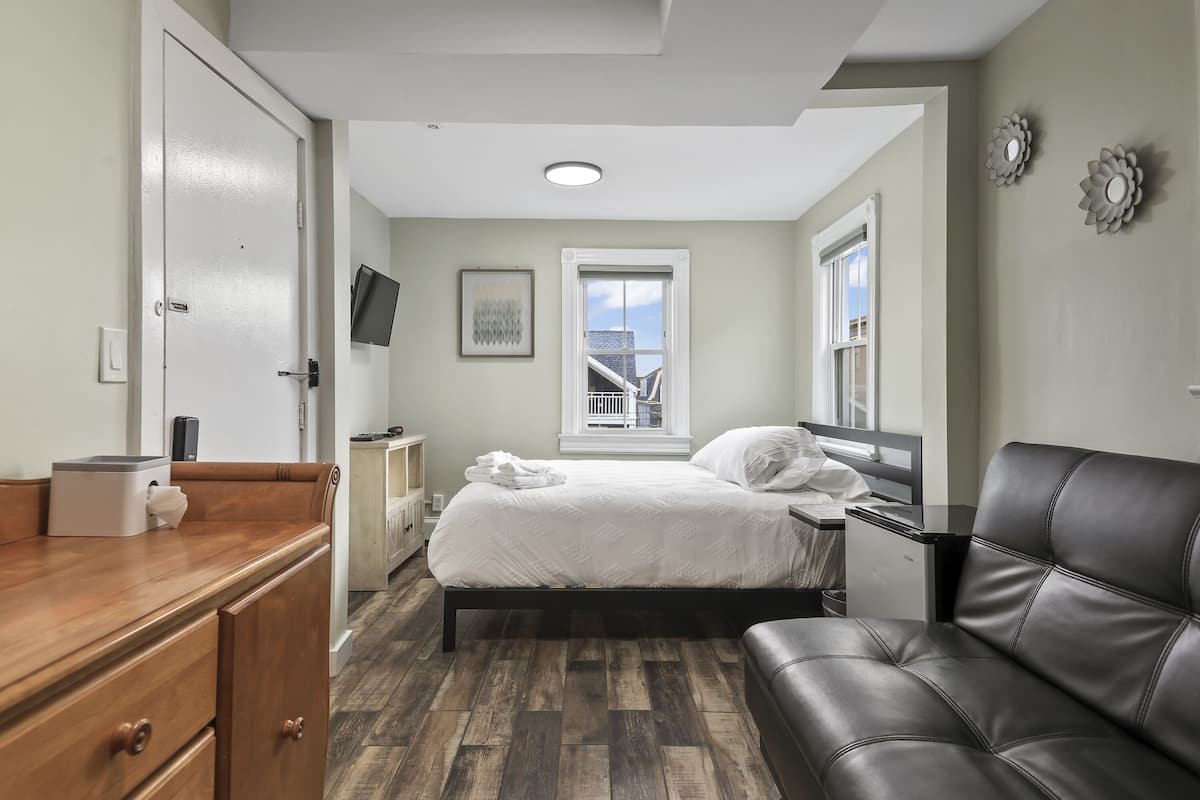 A bedroom with a bed, a desk, a chair, a dresser, and a window with a view.