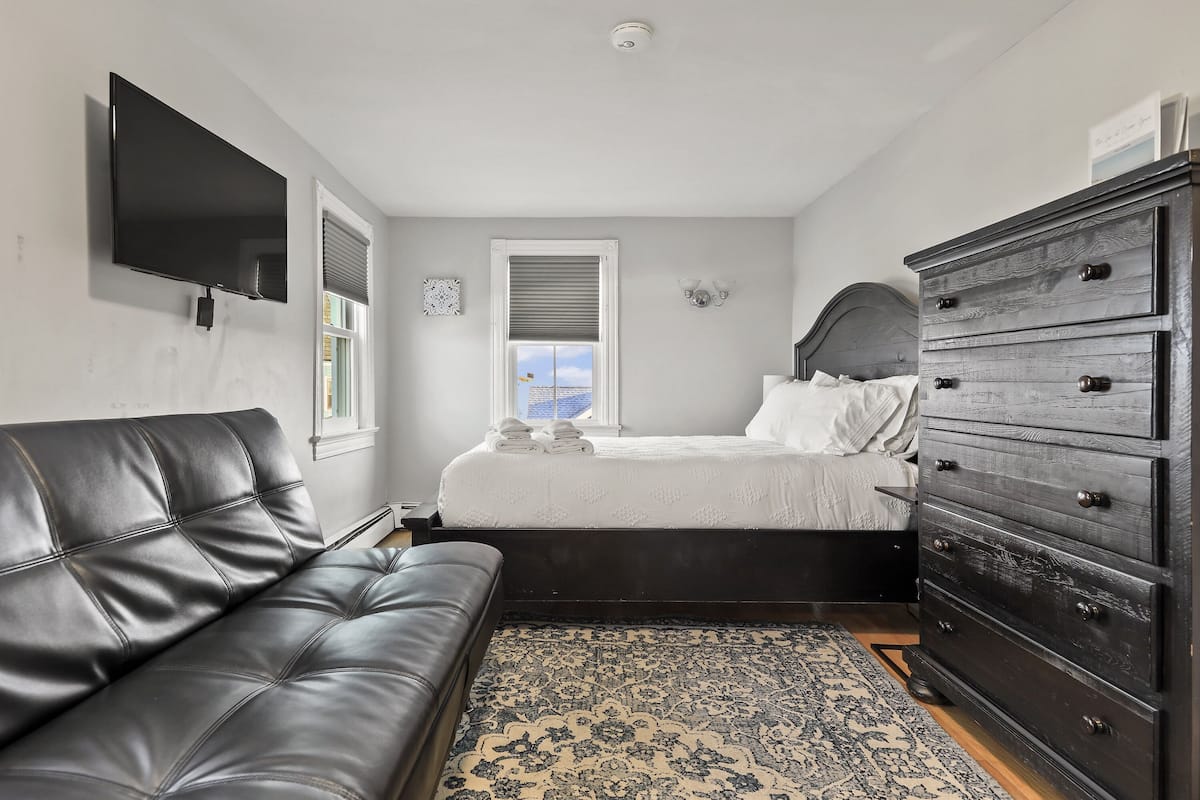 A bedroom with a bed, a dresser, a TV, and a couch.