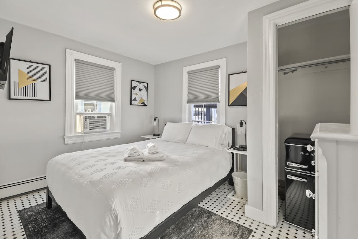 A hotel room with a large bed, two bedside tables, a wardrobe, and a bathroom with a shower.