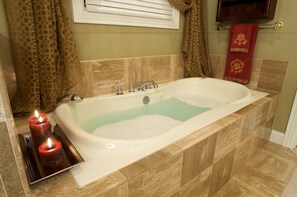 A bathroom with a bathtub, beige tiles, a window with blinds, and a towel rack with a red towel. - Southern Grace Bed & Breakfast (Brandenburg)