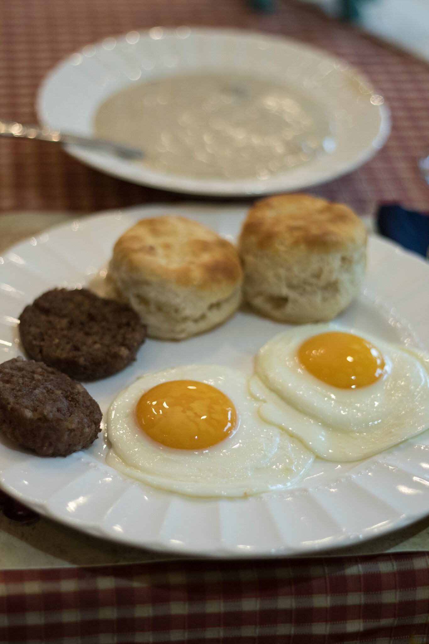 Un plato con huevos, salchichas y galletas sobre un mantel.