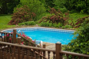 A swimming pool with a stone border and a wooden deck in a lush garden. - Southern Grace Bed & Breakfast (Brandenburg)