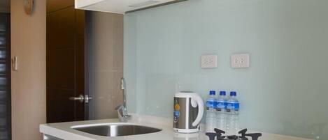 A modern kitchen with white cabinetry, a stainless steel sink, a kettle, and a gas stove.