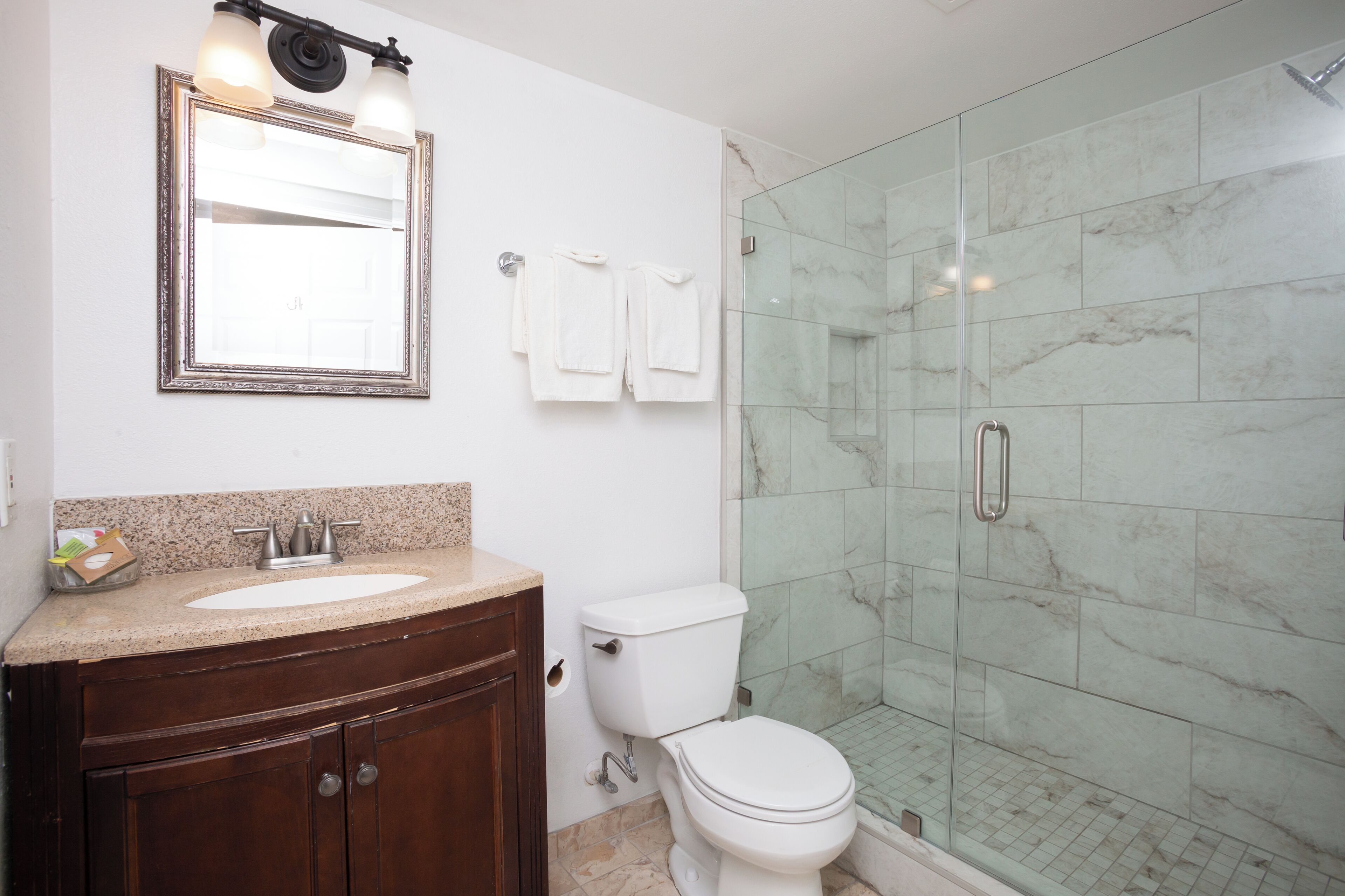 A bathroom with a marble shower, a sink, and a toilet.