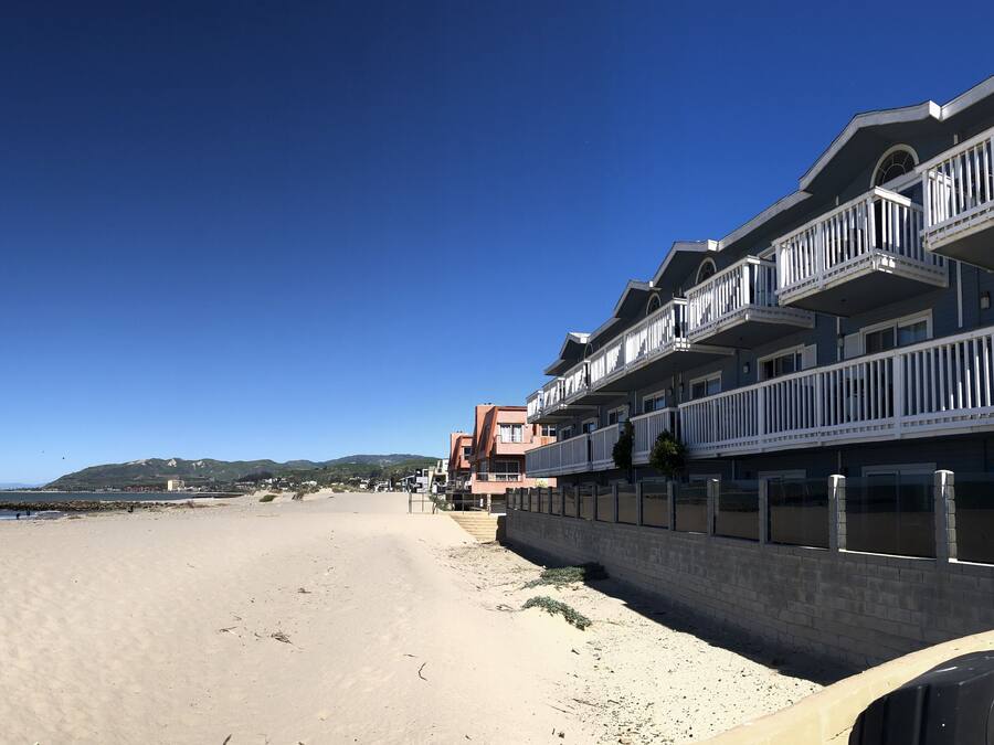 Um edifício à beira-mar com várias varandas, uma praia arenosa e um céu azul límpido.