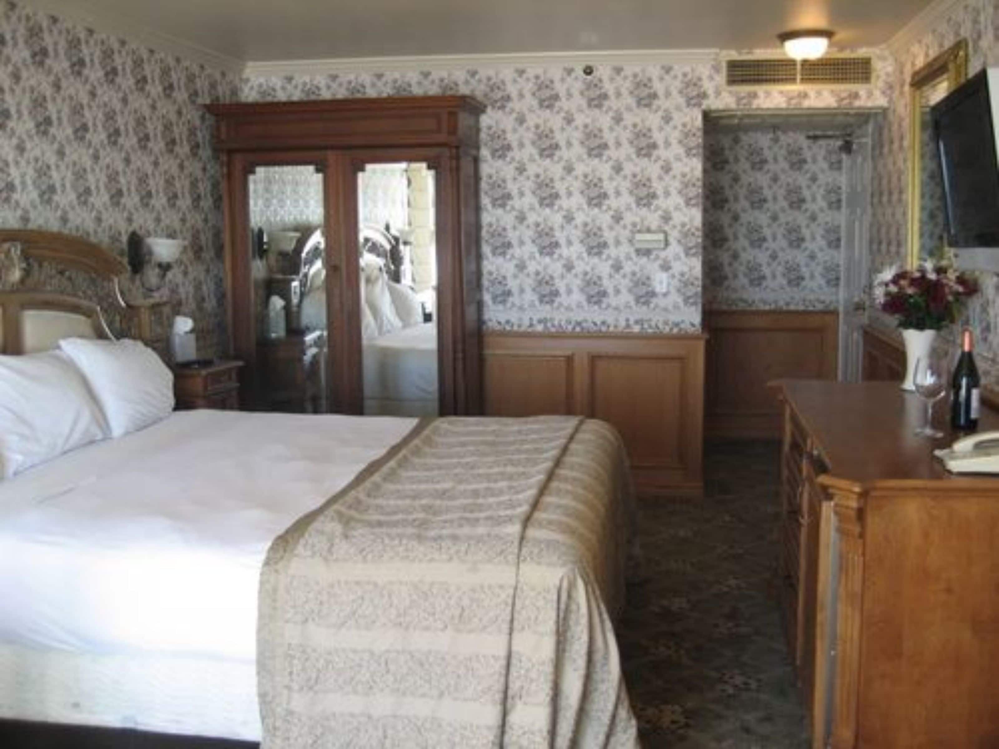 A hotel room with a bed, a dresser, a mirror, and a door leading to another room.