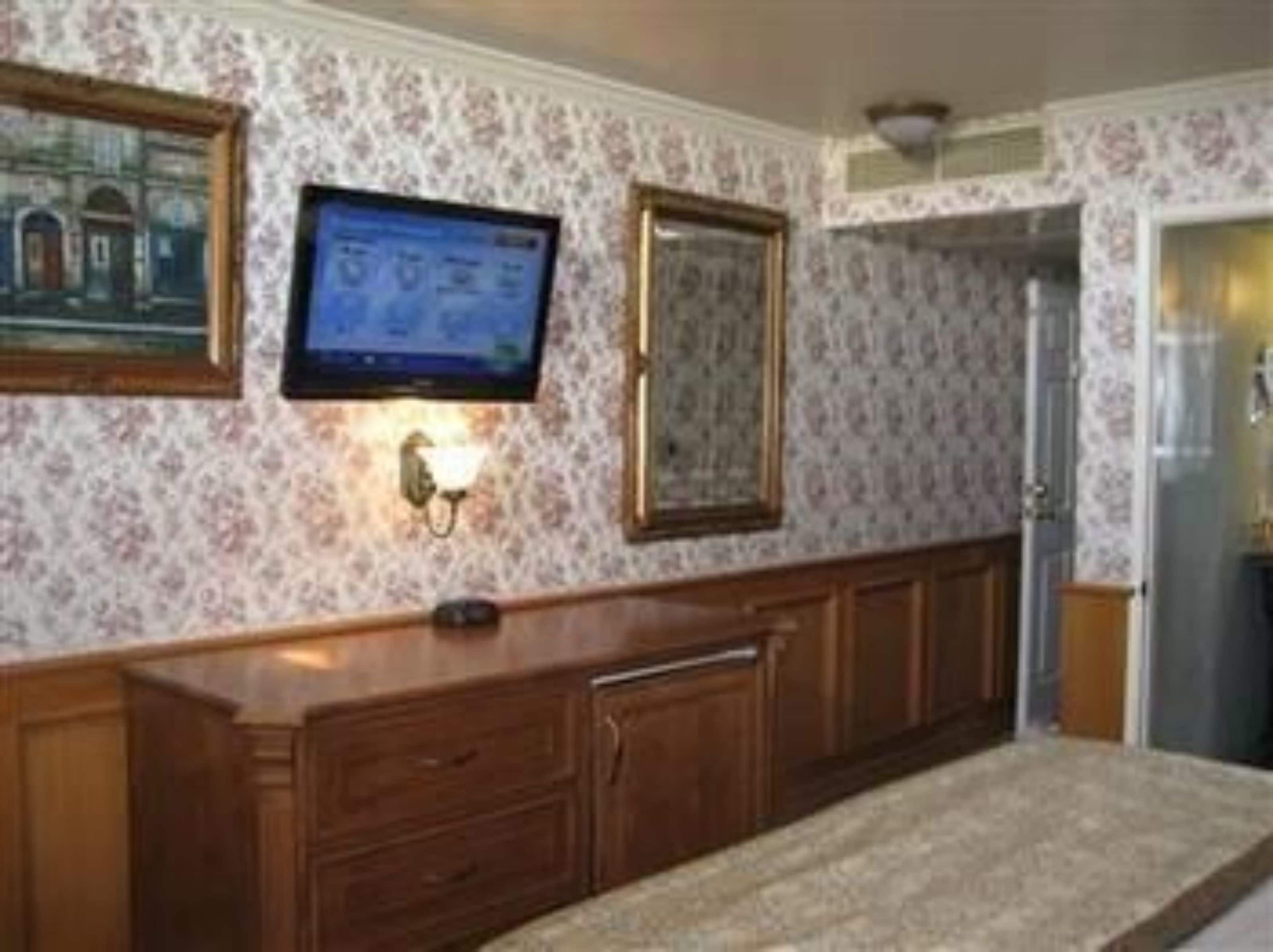 A hallway with a wooden bench, a television mounted on the wall, and a framed picture above it.