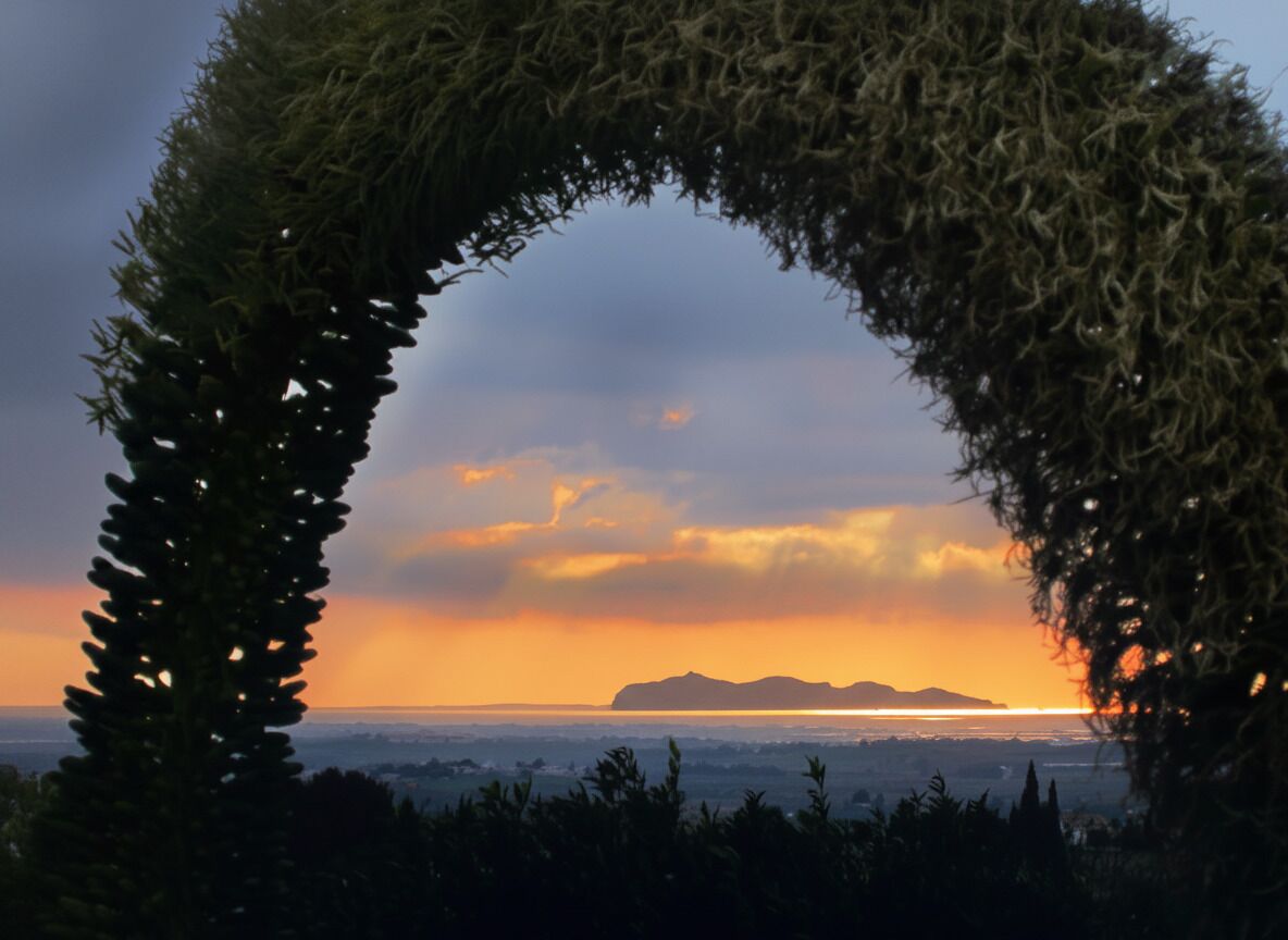 Une arche naturelle qui s’élève et encadre la vue sur un coucher de soleil au-dessus d’un paysage côtier.