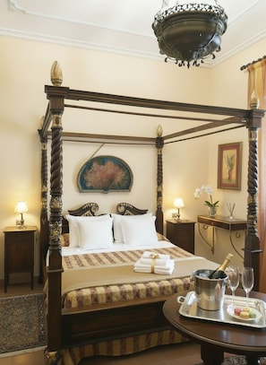 A four-poster bed with a canopy, a bedside table with a lamp, a framed picture on the wall, and a tray with a bottle and glasses on the floor. - Candalù - Villa Giardinata (Valderice)