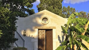 Un edificio con una ventana circular y una puerta, rodeado de follaje y una escalera.
