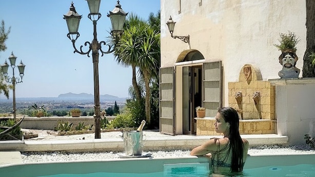 Ein Pool mit klarem Wasser, eine Person darin und ein Gebäude mit Tür und Fenstern im Hintergrund.