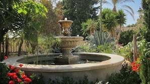 Ein mehrstufiger Springbrunnen, umgeben von üppigem Grün und blühenden Pflanzen.