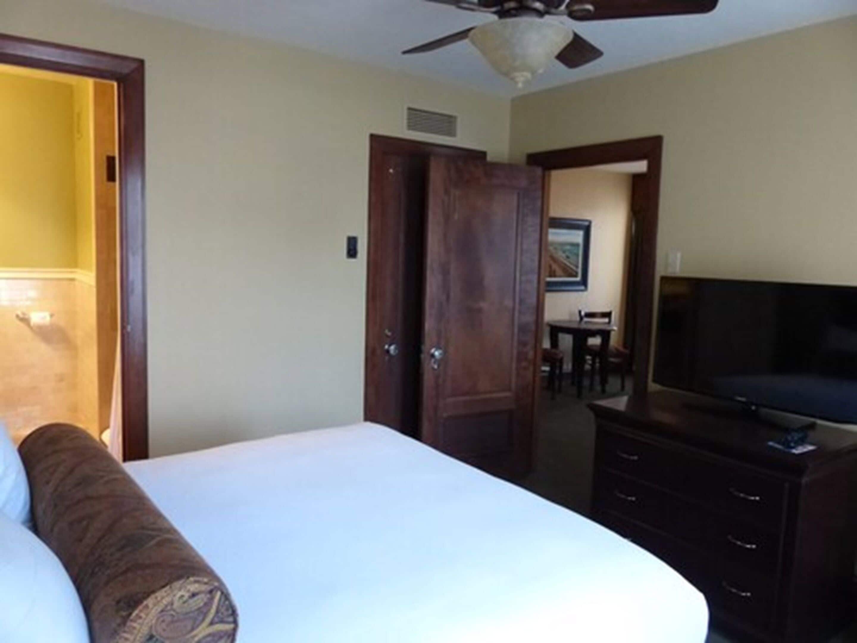 A hotel room with a bed, a television, a ceiling fan, and a wooden dresser.