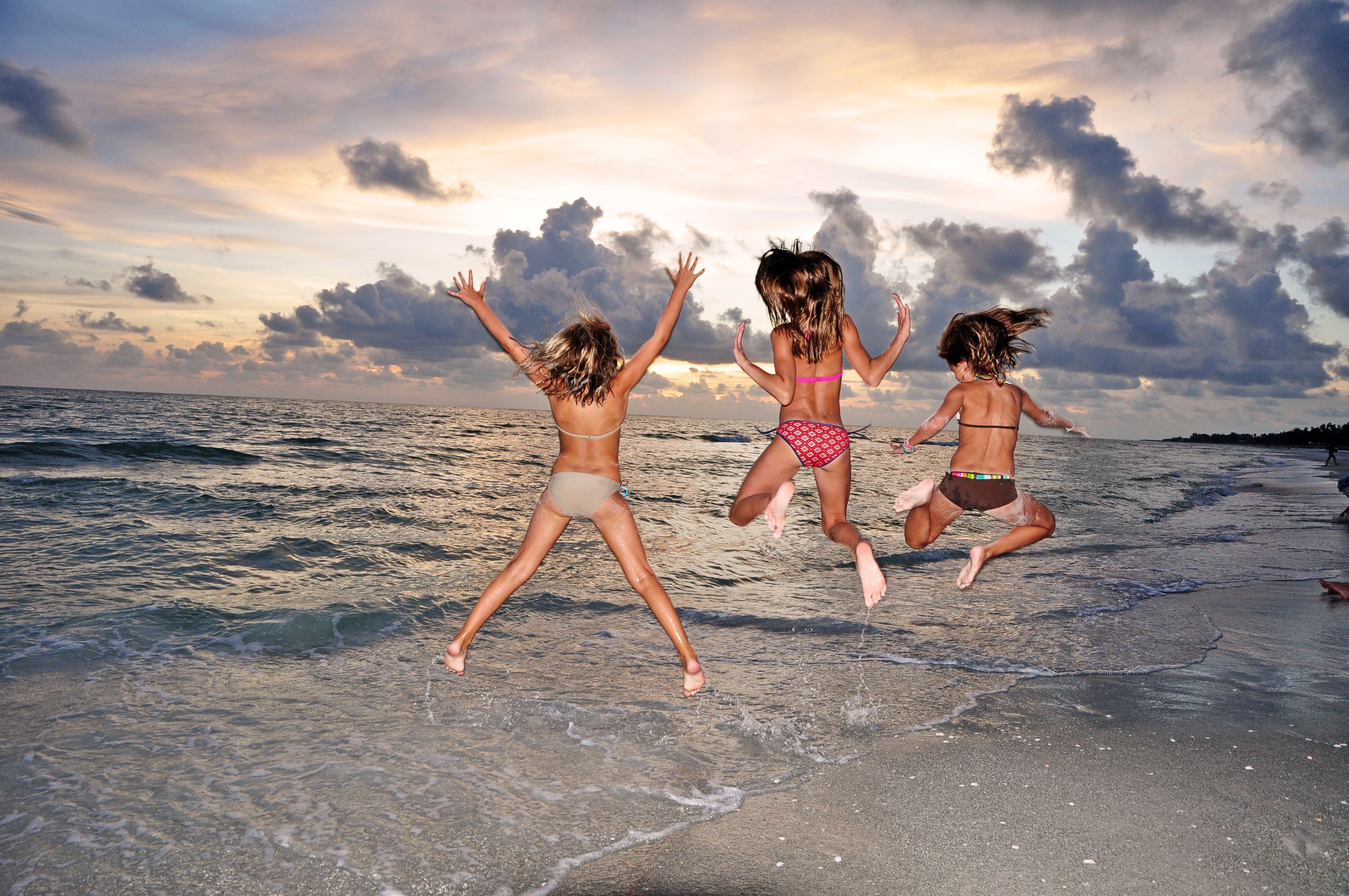 Tres personas saltando en una playa con el océano y un cielo nublado al fondo.
