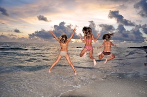 Three people jumping on a beach with the ocean and a cloudy sky in the background. - Beach Castle Resort by RVA (Longboat Key)