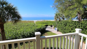 A view from a balcony overlooking a well-maintained garden with a pathway leading to a beach.