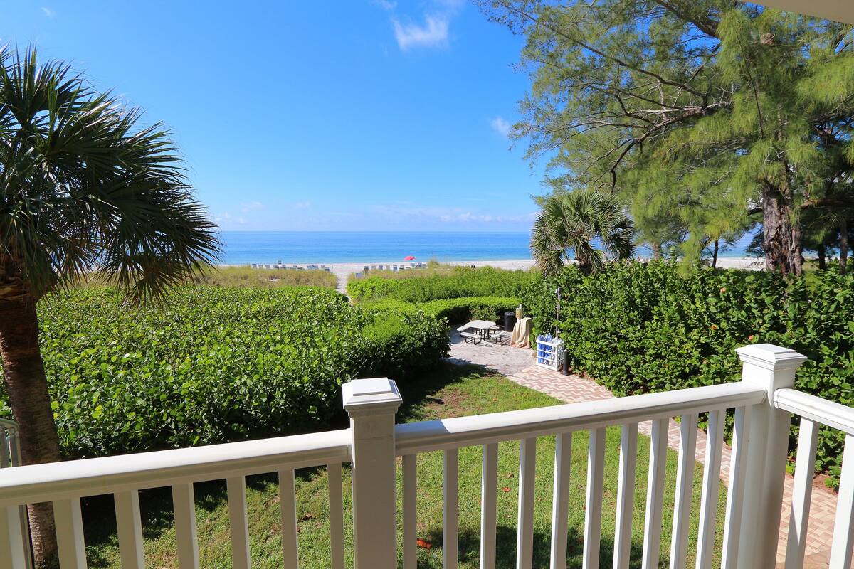 A view from a balcony overlooking a well-maintained garden with a pathway leading to a beach.