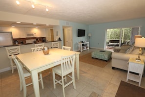 A spacious living area with a dining table, chairs, a sofa, and a TV mounted on the wall.